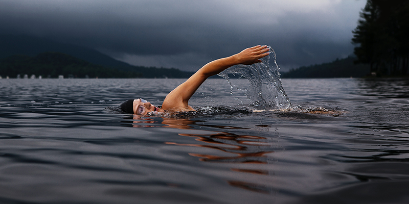 A man swimming in a lake with dark clouds in the background