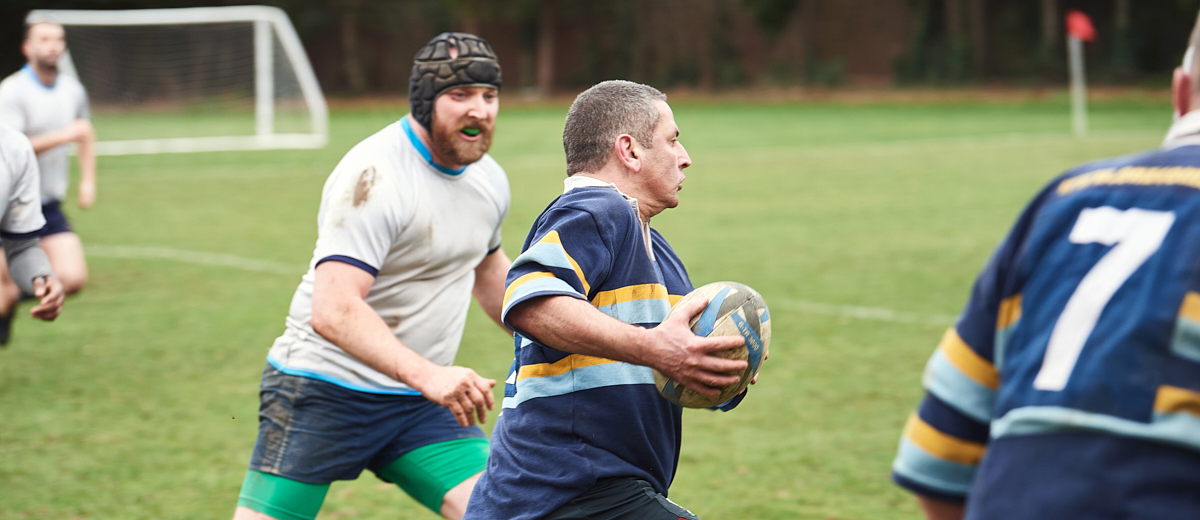 A man running with the ball during a rugby match, another player about to tackle him