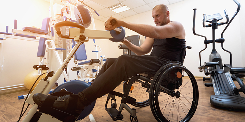 A man sitting in a wheelchair and using a hand cycle in a gym