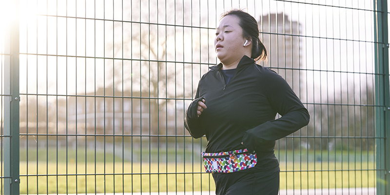 A woman running outside in a park next to a fence