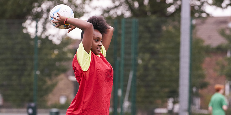 A teenage girl holding a ball above her head with two hands about to throw