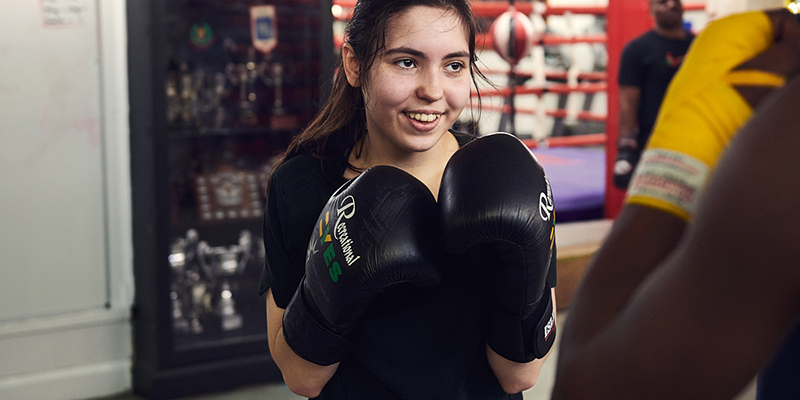 A young woman wearing boxing gloves and smiling
