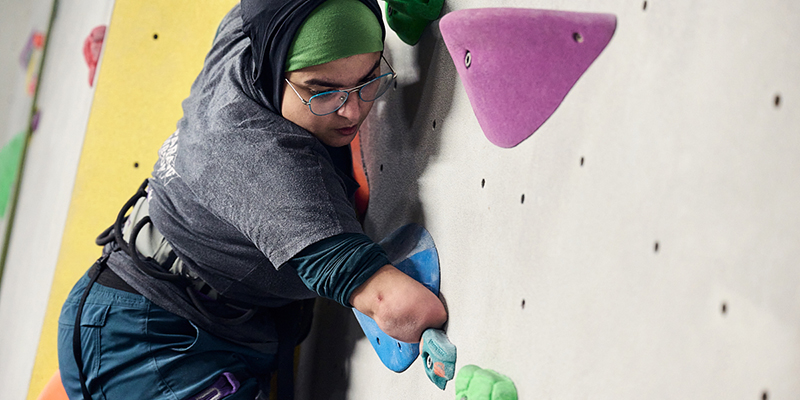 A young woman with a right arm amputation climbing on an indoor climbing wall