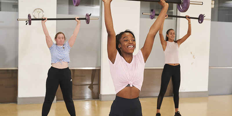 Three young women lifting bar weights in an exercise class