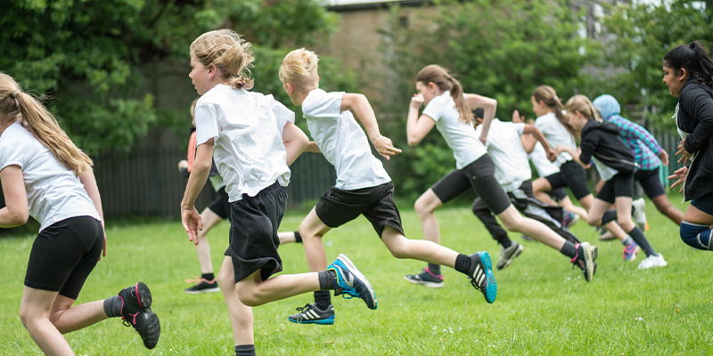 A group of children in a PE lesson running across a field