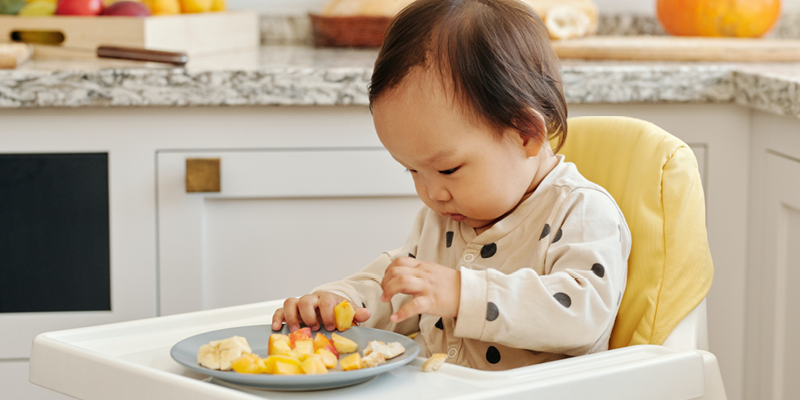 A young child in a high chair eating a plate of fruit