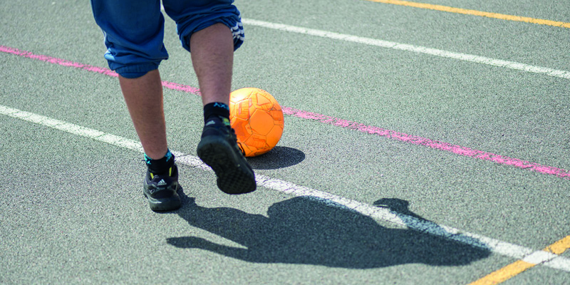 Two feet kicking a football on a concrete playground