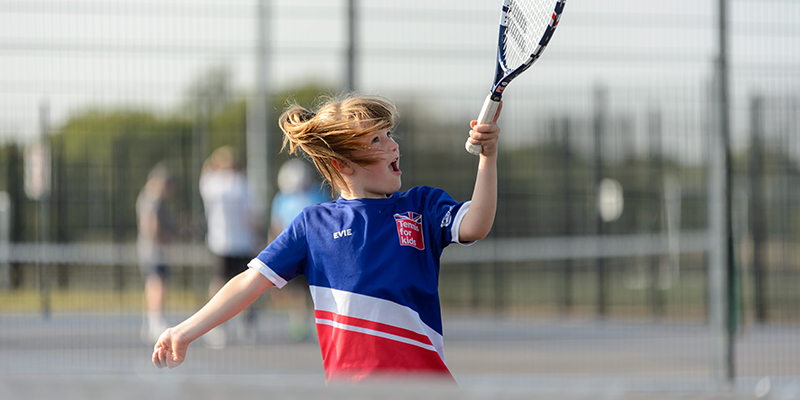 A young girl hitting a tennis ball with a racket