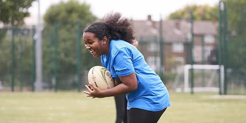 A teenage girl smiling as she catches a rugby ball