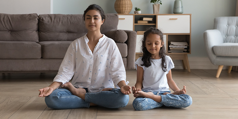 A woman and a preschool child meditating seated in lotus position on floor