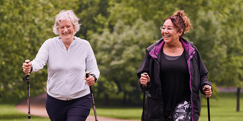 Two older women walking in a park with walking poles