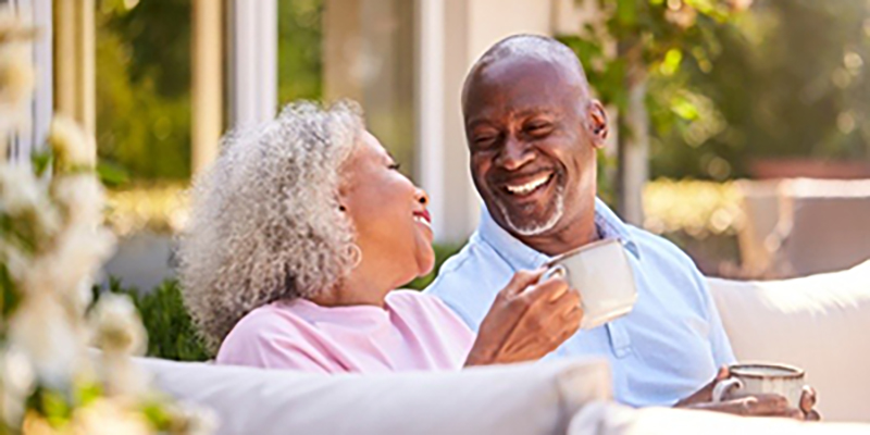 An older couple sit looking at each other and smiling